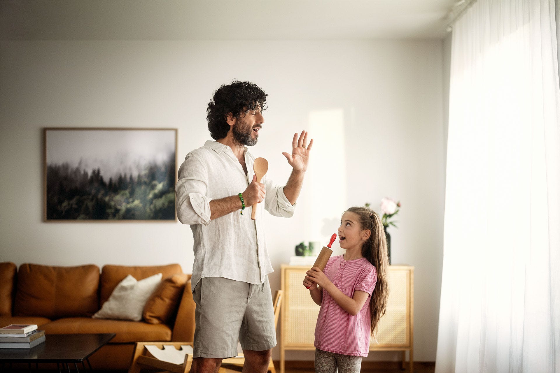 Isä ja tytär laulavat yhdessä iloisesti kotona, pitäen keittiövälineitä mikrofoneina.