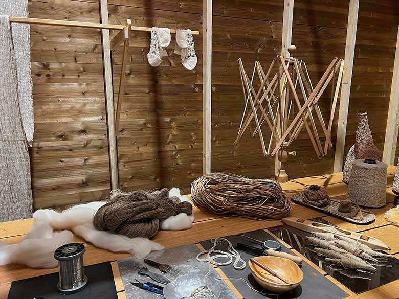 Puupöydällä villaa, lankoja, punottuja materiaaleja ja puisia käsityövälineitä.