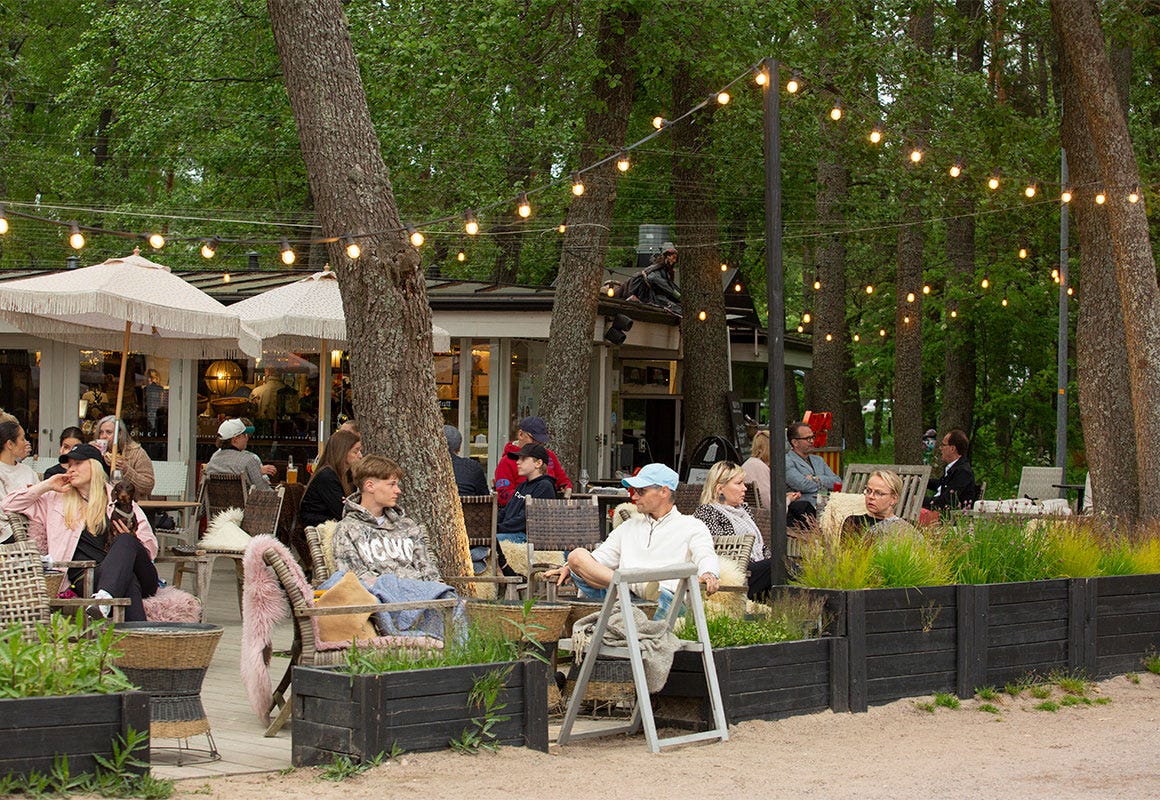 Ihmisi&auml; istuu Kahvila Kasinonrannan ja Lauttasaari Paviljongin terassilla puiden ja valoketjujen alla.
