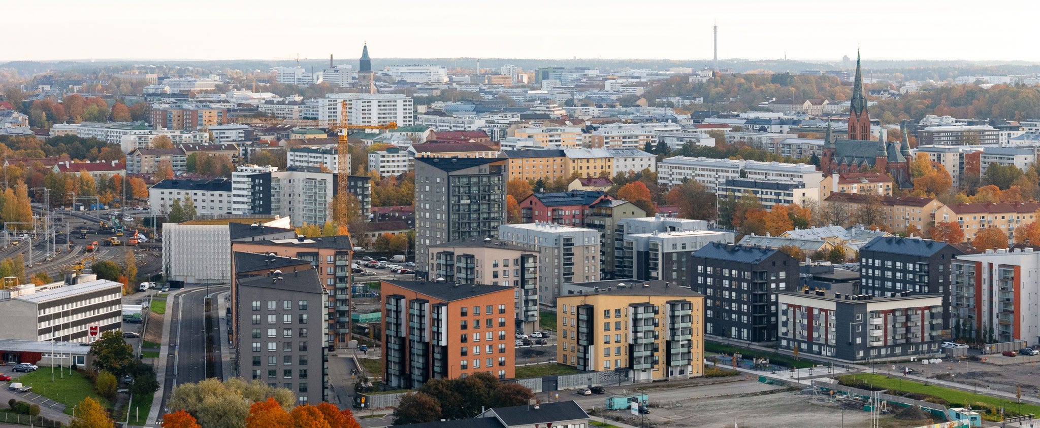 Ilmakuva Turun Kirstinpuiston alueesta. Kuvassa näkyy uusia kerrostaloja, rakennustyömaita ja kaupungin siluetti, mukaan lukien kirkontorni. Syksyinen maisema, jossa rakennukset ja puut hehkuvat lämpimissä sävyissä.