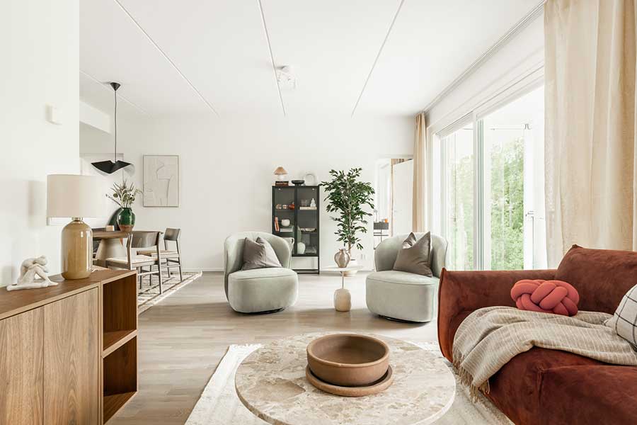 Valoisa olohuone, jossa korkea huonekorkeus, suuret ikkunat ja näkymä vehreälle pihalle.