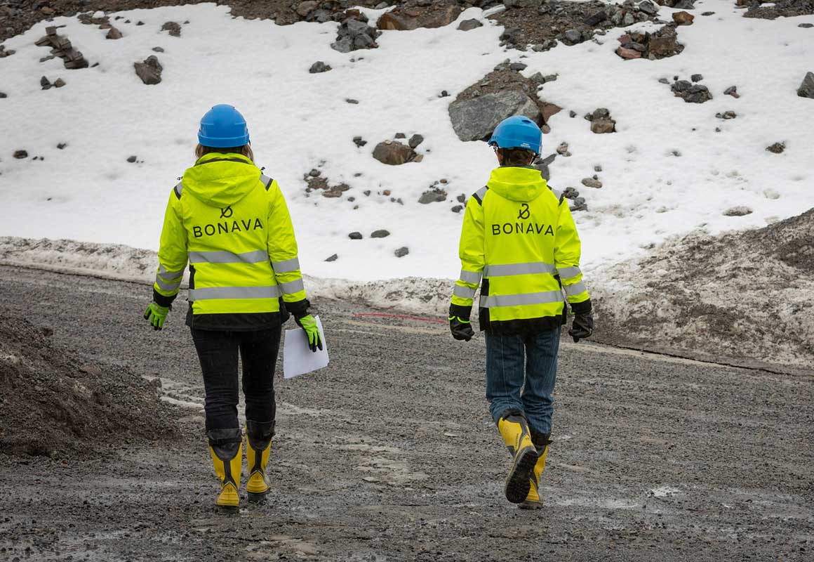 Kaksi Bonavan työvaatteisiin ja kypäriin pukeutunutta rakennusalan ammattilaista kävelee työmaalla talvisessa ympäristössä.