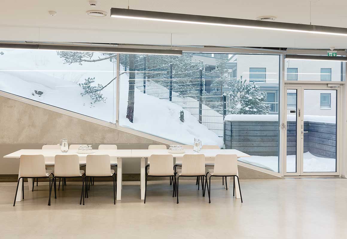 Kruunuvuorenrannan yhteinen juhlatila, jossa pitkä ruokapöytä ja suuret ikkunat talviseen piha- ja metsämaisemaan.