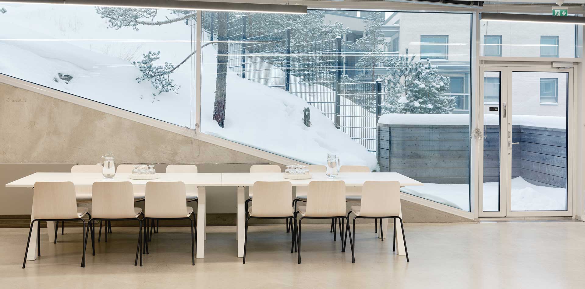 Kruunuvuorenrannan yhteinen juhlatila, jossa pitkä ruokapöytä ja suuret ikkunat talviseen piha- ja metsämaisemaan.