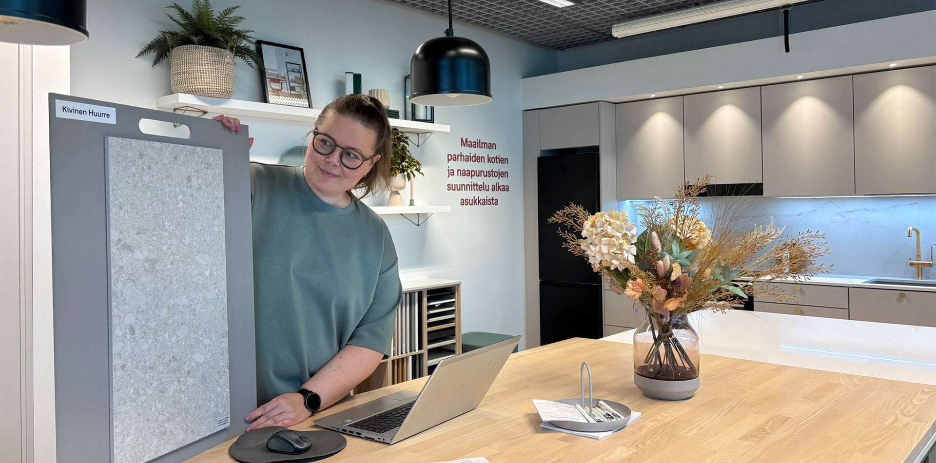 Nainen esittelee suurta kivilaattamallia keittiön suunnittelutilassa pöydän ääressä.