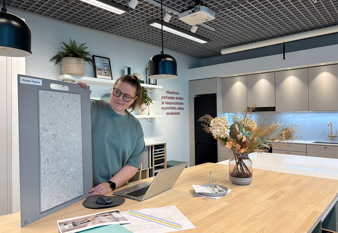 Nainen esittelee suurta kivilaattamallia keittiön suunnittelutilassa pöydän ääressä.