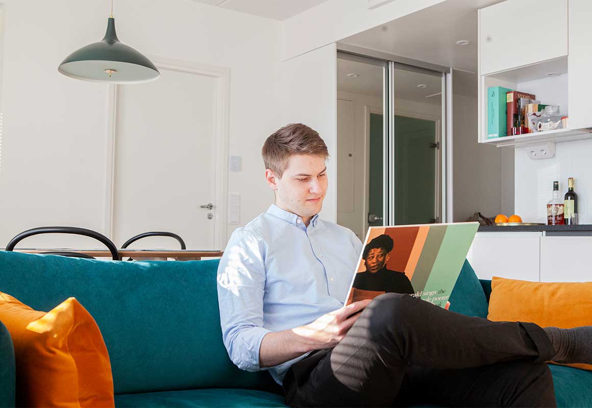 Mies istuu turkoosilla sohvalla ja katselee vinyylilevyn kantta modernissa olohuoneessa.