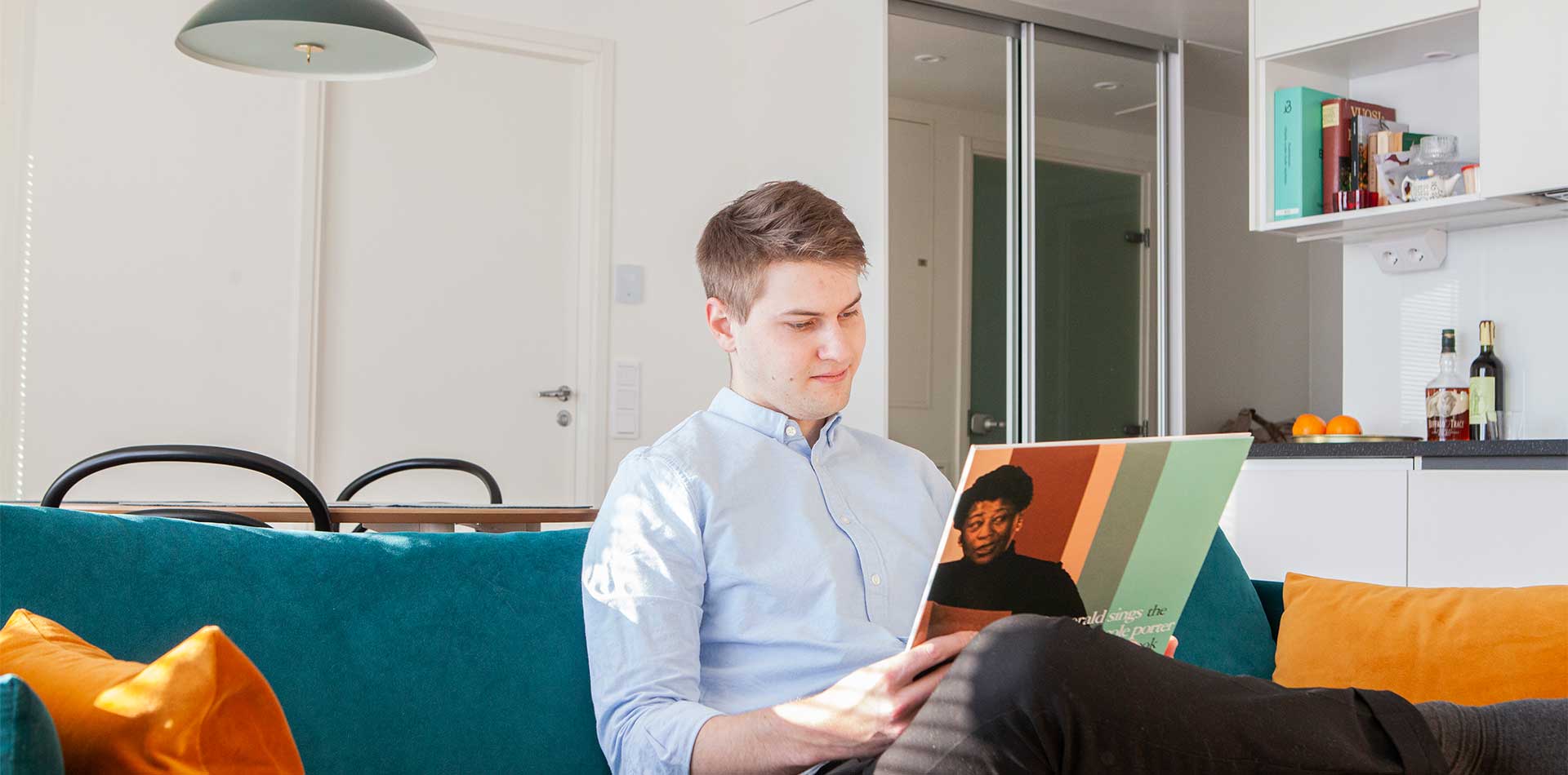 Mies istuu turkoosilla sohvalla ja katselee vinyylilevyn kantta modernissa olohuoneessa.