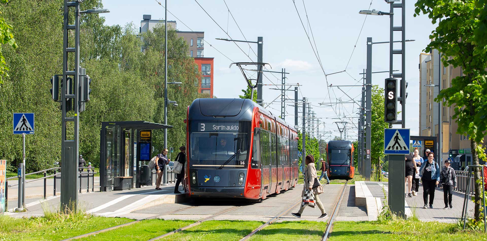 Tampereen ratikka pysähtyy Kalevanrinteen pysäkillä – matkustajia nousee ja ylittää raidetta kaupunkimaisessa ympäristössä.