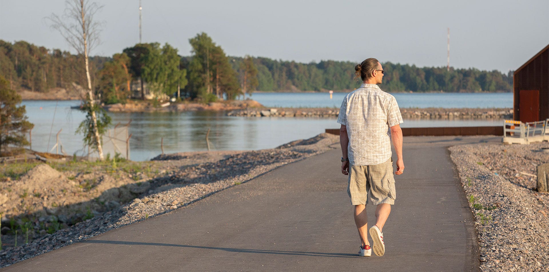 Henkilö kävelee ilta-auringossa rantatietä pitkin merimaisemien äärellä.