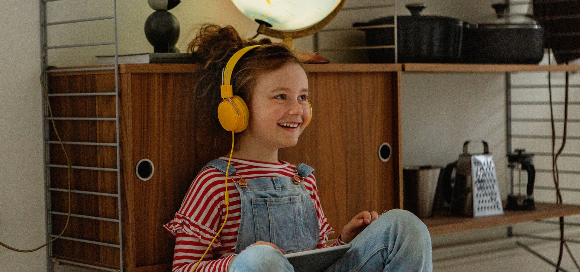 Lapsi kuuntelee kuulokkeilla tabletista sisältöä kotona – lämmin ja rauhallinen tunnelma.