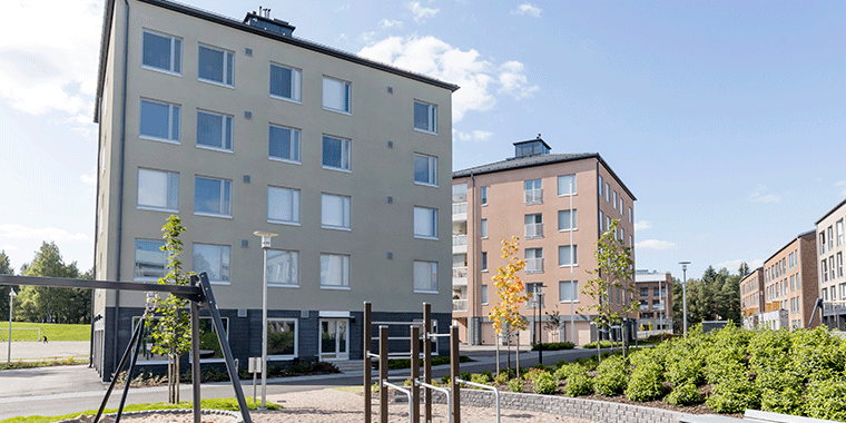 Haagan Huvilat - Moderni kerrostaloalue, jossa vaaleasävyisiä rakennuksia, vehreää piha-aluetta ja leikkipaikka. Etualalla kiipeilyteline ja keinu, taustalla sininen taivas ja vehreä maisema.