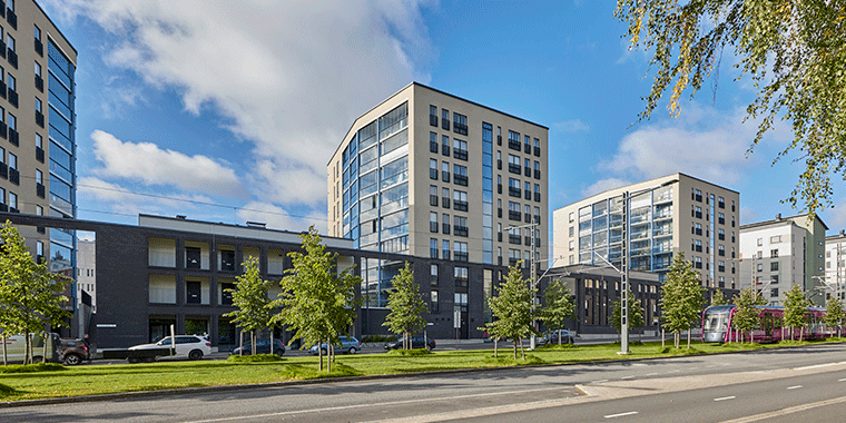 Moderni Kalevan Paletti -kotikortteli Tampereella. Kuvassa 8–9-kerroksiset kerrostalot, joiden lasitetut parvekkeet heijastavat taivasta. Vehreä katualue ja raitiovaunu lisäävät kaupunkimaista tunnelmaa.