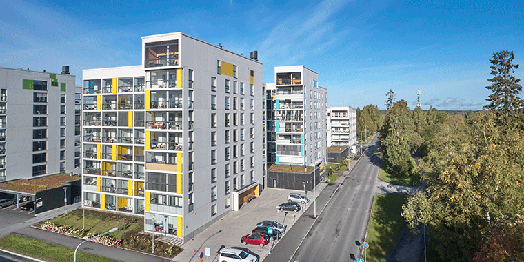 Lielahden kotikorttelin moderneja kerrostaloja Tampereella. Etualalla kahdeksankerroksinen talo, jonka julkisivua elävöittävät keltaiset yksityiskohdat ja suuret lasitetut parvekkeet. Kadun toisella puolella vehreää metsämaisemaa.