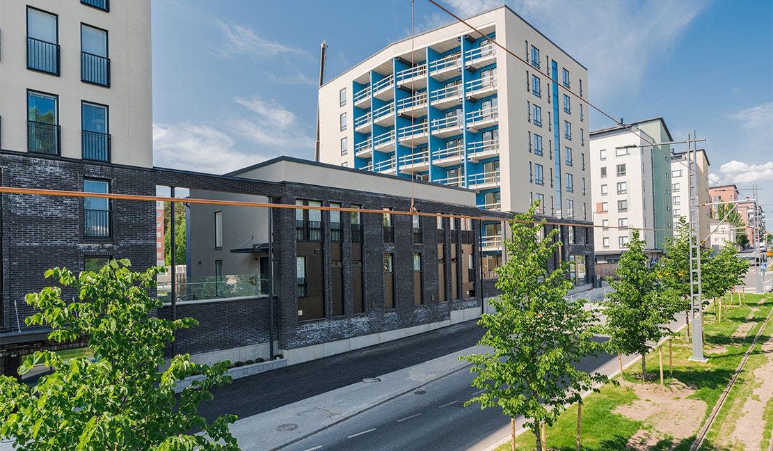 Kalevan Paletti, Tampere Kalevan Paletin modernia kaupunkirakentamista Tampereella. Kuvassa korkeita, lasitettuja kerrostaloja sekä matalampi rakennus tummalla tiiliverhouksella. Etualalla puurivistö ja raitiovaunukiskot vihreässä kaupunkiympäristössä.