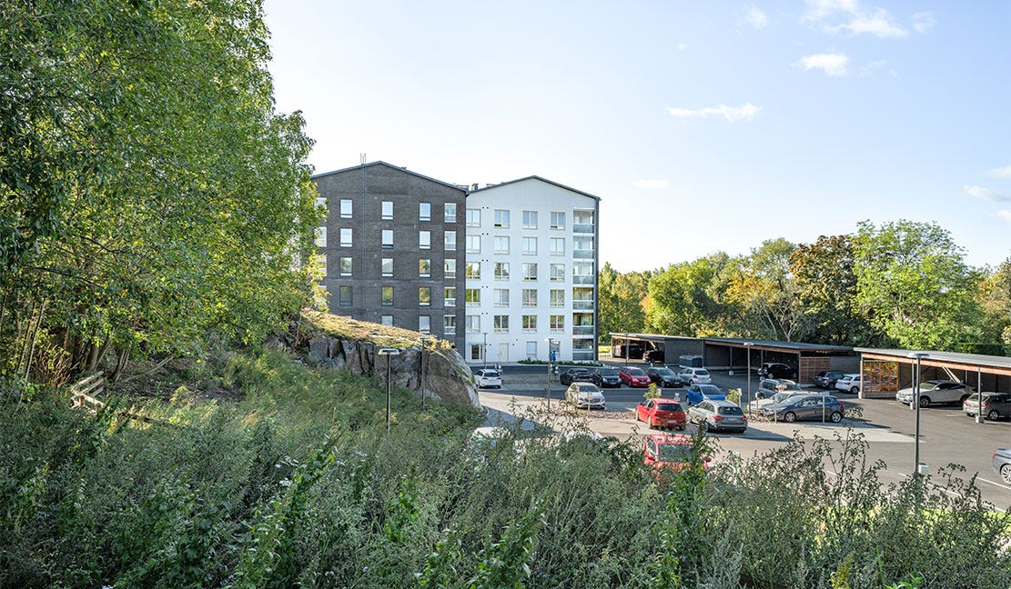 Vähäheikkilän Huvitus, Turku Vähäheikkilän Huvituksen modernit kerrostalot sulautuvat vehreään ympäristöön. Etualalla kallioista maastoa ja vihreää kasvillisuutta, taustalla asukkaiden pysäköintialue katoksineen.