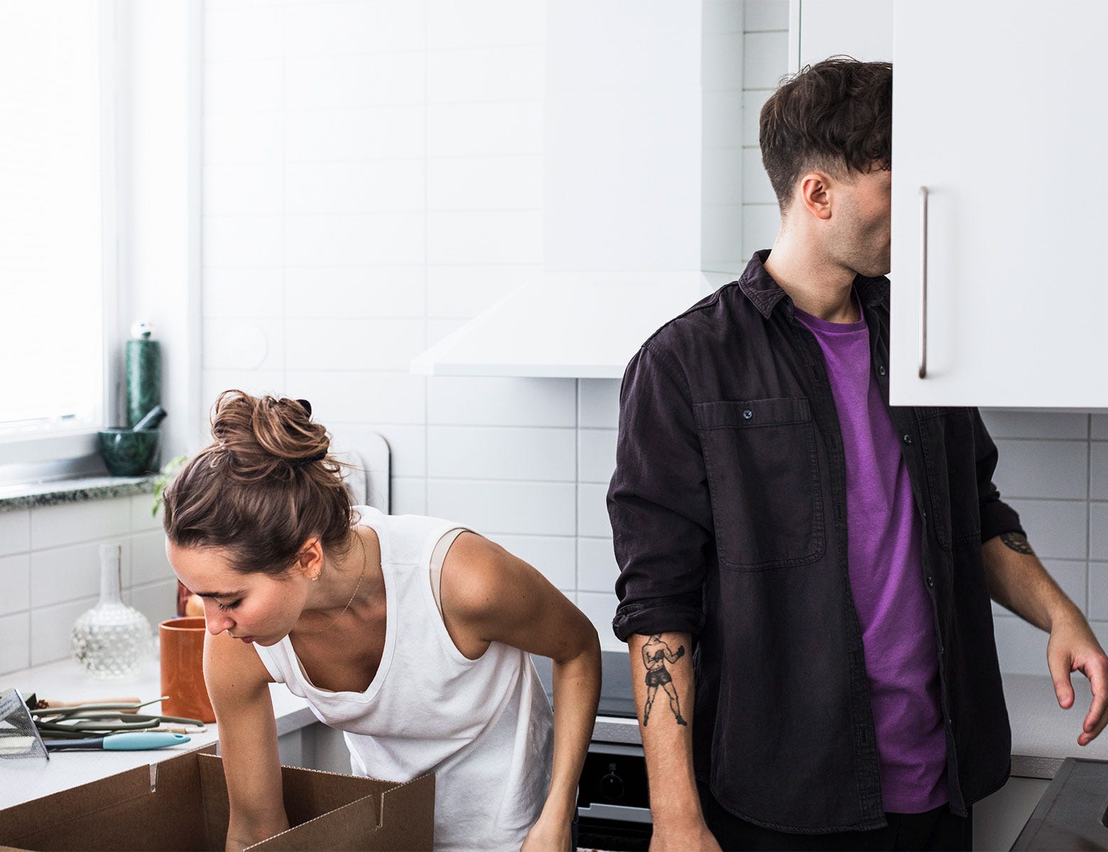 Nuori pariskunta purkaa muuttolaatikoita valkoisessa keittiössä. Nainen kumartuu ottamaan tavaroita laatikosta, kun taas mies etsii jotain keittiökaapista.