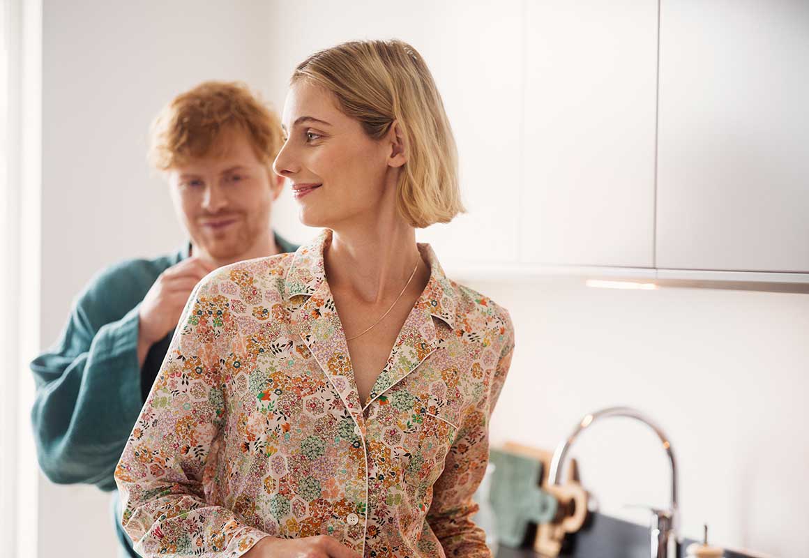 Nainen seisoo keittiössä, ja hänen takanaan seisoo mies .